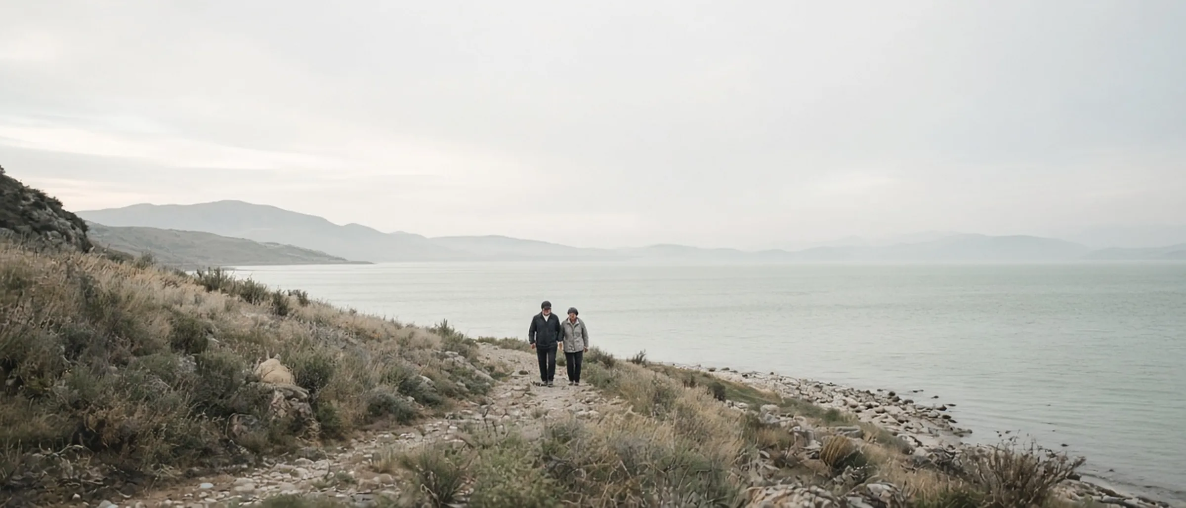 Two people walking a lakeside trail under a wide sky.